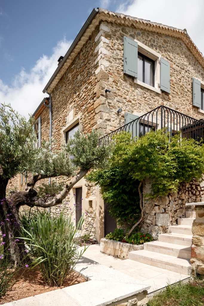 Rénovation complète d’une maison de famille – Drôme
Nichée au cœur des paysages de la Drôme, cette maison a fait l’objet d’une rénovation intégrale. Le projet a consisté à redonner vie à une bâtisse aux volumes autrefois fermés et cloisonnés, pour en révéler tout le potentiel architectural et spatial.
L’intervention a porté sur l’ensemble de l’enveloppe : les façades ont été restaurées, les ouvertures repensées et créées pour offrir de nouveaux cadrages sur le paysage, mettant en valeur la pierre existante et la richesse du contexte environnant.
À l’intérieur, les espaces ont été entièrement réorganisés. Le plan initial, fragmenté et contraint, a laissé place à des enchaînements fluides, où les pièces dialoguent entre elles et s’ouvrent généreusement sur l’extérieur. Chaque ouverture devient un tableau vivant, cadrant une portion de nature : champs de blé, forêt, lumière changeante.
Le cœur de la maison se structure autour de volumes entremêlés. Une cheminée centrale, élément à la fois architectural et domestique, relie les grands volumes de la cuisine en double hauteur et le salon, plus intime et chaleureux. Dans une autre aile, à l’étage, une seconde cuisine a été aménagée. Elle prolonge l’esprit du projet : fonctionnalité discrète, ouverture maîtrisée, cadrages sensibles sur le paysage.
Les ambiances varient selon les espaces : une chambre se déploie autour d’un vide intérieur, jouant avec les hauteurs et les couleurs ; le salon TV, équipé d’une bibliothèque et de rangements intégrés, offre un lieu de retrait, propice au calme tout en restant connecté à l’extérieur.
Le choix des matériaux renforce l’identité sobre et chaleureuse du lieu : pierre naturelle, travertin, parquet en chêne et surfaces en solid surface s’équilibrent pour créer une atmosphère douce, intemporelle et raffinée.
Les ouvertures ont été dessinées pour favoriser la lumière naturelle et créer des liens visuels avec le paysage, tout en accompagnant les usages quotidiens. À l’extérieur, une piscine s’insère discrètement dans le jardin paysager, entourée de terrasses orientées pour profiter du soleil tout au long de la journée. La maison se fond progressivement dans son environnement, entre les cultures et les bois, dans un dialogue apaisé avec le site.
Enfin, les espaces de nuit, regroupés dans une aile plus en retrait, assurent calme et sérénité. Ils sont complétés par une salle de sport et un second salon dédié aux plus jeunes, pour que chacun puisse vivre la maison à son rythme, en toute liberté.