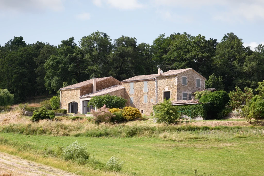 Rénovation complète d’une maison de famille – Drôme
Nichée au cœur des paysages de la Drôme, cette maison a fait l’objet d’une rénovation intégrale. Le projet a consisté à redonner vie à une bâtisse aux volumes autrefois fermés et cloisonnés, pour en révéler tout le potentiel architectural et spatial.
L’intervention a porté sur l’ensemble de l’enveloppe : les façades ont été restaurées, les ouvertures repensées et créées pour offrir de nouveaux cadrages sur le paysage, mettant en valeur la pierre existante et la richesse du contexte environnant.
À l’intérieur, les espaces ont été entièrement réorganisés. Le plan initial, fragmenté et contraint, a laissé place à des enchaînements fluides, où les pièces dialoguent entre elles et s’ouvrent généreusement sur l’extérieur. Chaque ouverture devient un tableau vivant, cadrant une portion de nature : champs de blé, forêt, lumière changeante.
Le cœur de la maison se structure autour de volumes entremêlés. Une cheminée centrale, élément à la fois architectural et domestique, relie les grands volumes de la cuisine en double hauteur et le salon, plus intime et chaleureux. Dans une autre aile, à l’étage, une seconde cuisine a été aménagée. Elle prolonge l’esprit du projet : fonctionnalité discrète, ouverture maîtrisée, cadrages sensibles sur le paysage.
Les ambiances varient selon les espaces : une chambre se déploie autour d’un vide intérieur, jouant avec les hauteurs et les couleurs ; le salon TV, équipé d’une bibliothèque et de rangements intégrés, offre un lieu de retrait, propice au calme tout en restant connecté à l’extérieur.
Le choix des matériaux renforce l’identité sobre et chaleureuse du lieu : pierre naturelle, travertin, parquet en chêne et surfaces en solid surface s’équilibrent pour créer une atmosphère douce, intemporelle et raffinée.
Les ouvertures ont été dessinées pour favoriser la lumière naturelle et créer des liens visuels avec le paysage, tout en accompagnant les usages quotidiens. À l’extérieur, une piscine s’insère discrètement dans le jardin paysager, entourée de terrasses orientées pour profiter du soleil tout au long de la journée. La maison se fond progressivement dans son environnement, entre les cultures et les bois, dans un dialogue apaisé avec le site.
Enfin, les espaces de nuit, regroupés dans une aile plus en retrait, assurent calme et sérénité. Ils sont complétés par une salle de sport et un second salon dédié aux plus jeunes, pour que chacun puisse vivre la maison à son rythme, en toute liberté.