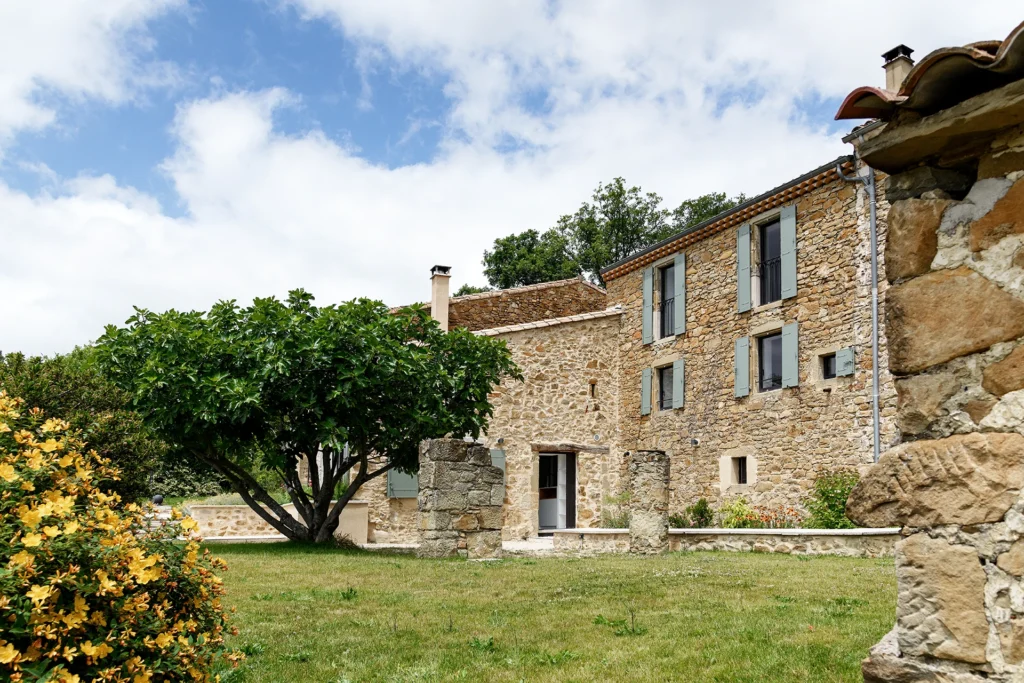 Rénovation complète d’une maison de famille – Drôme
Nichée au cœur des paysages de la Drôme, cette maison a fait l’objet d’une rénovation intégrale. Le projet a consisté à redonner vie à une bâtisse aux volumes autrefois fermés et cloisonnés, pour en révéler tout le potentiel architectural et spatial.
L’intervention a porté sur l’ensemble de l’enveloppe : les façades ont été restaurées, les ouvertures repensées et créées pour offrir de nouveaux cadrages sur le paysage, mettant en valeur la pierre existante et la richesse du contexte environnant.
À l’intérieur, les espaces ont été entièrement réorganisés. Le plan initial, fragmenté et contraint, a laissé place à des enchaînements fluides, où les pièces dialoguent entre elles et s’ouvrent généreusement sur l’extérieur. Chaque ouverture devient un tableau vivant, cadrant une portion de nature : champs de blé, forêt, lumière changeante.
Le cœur de la maison se structure autour de volumes entremêlés. Une cheminée centrale, élément à la fois architectural et domestique, relie les grands volumes de la cuisine en double hauteur et le salon, plus intime et chaleureux. Dans une autre aile, à l’étage, une seconde cuisine a été aménagée. Elle prolonge l’esprit du projet : fonctionnalité discrète, ouverture maîtrisée, cadrages sensibles sur le paysage.
Les ambiances varient selon les espaces : une chambre se déploie autour d’un vide intérieur, jouant avec les hauteurs et les couleurs ; le salon TV, équipé d’une bibliothèque et de rangements intégrés, offre un lieu de retrait, propice au calme tout en restant connecté à l’extérieur.
Le choix des matériaux renforce l’identité sobre et chaleureuse du lieu : pierre naturelle, travertin, parquet en chêne et surfaces en solid surface s’équilibrent pour créer une atmosphère douce, intemporelle et raffinée.
Les ouvertures ont été dessinées pour favoriser la lumière naturelle et créer des liens visuels avec le paysage, tout en accompagnant les usages quotidiens. À l’extérieur, une piscine s’insère discrètement dans le jardin paysager, entourée de terrasses orientées pour profiter du soleil tout au long de la journée. La maison se fond progressivement dans son environnement, entre les cultures et les bois, dans un dialogue apaisé avec le site.
Enfin, les espaces de nuit, regroupés dans une aile plus en retrait, assurent calme et sérénité. Ils sont complétés par une salle de sport et un second salon dédié aux plus jeunes, pour que chacun puisse vivre la maison à son rythme, en toute liberté.