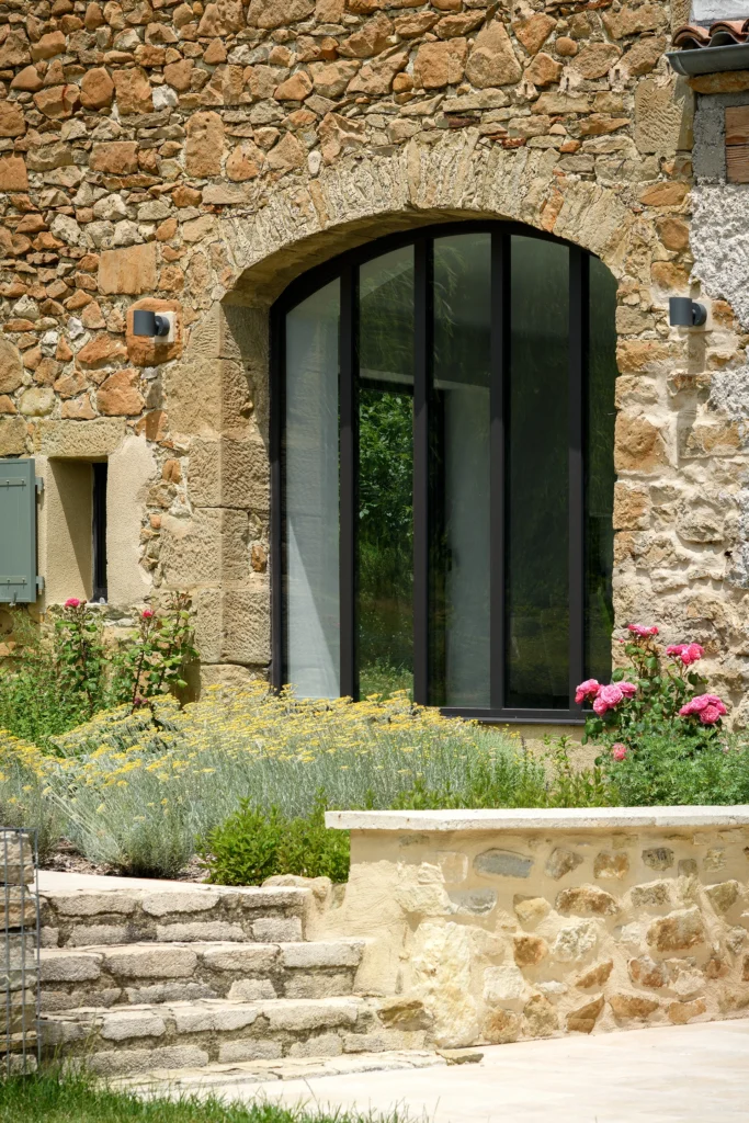 Rénovation complète d’une maison de famille – Drôme
Nichée au cœur des paysages de la Drôme, cette maison a fait l’objet d’une rénovation intégrale. Le projet a consisté à redonner vie à une bâtisse aux volumes autrefois fermés et cloisonnés, pour en révéler tout le potentiel architectural et spatial.
L’intervention a porté sur l’ensemble de l’enveloppe : les façades ont été restaurées, les ouvertures repensées et créées pour offrir de nouveaux cadrages sur le paysage, mettant en valeur la pierre existante et la richesse du contexte environnant.
À l’intérieur, les espaces ont été entièrement réorganisés. Le plan initial, fragmenté et contraint, a laissé place à des enchaînements fluides, où les pièces dialoguent entre elles et s’ouvrent généreusement sur l’extérieur. Chaque ouverture devient un tableau vivant, cadrant une portion de nature : champs de blé, forêt, lumière changeante.
Le cœur de la maison se structure autour de volumes entremêlés. Une cheminée centrale, élément à la fois architectural et domestique, relie les grands volumes de la cuisine en double hauteur et le salon, plus intime et chaleureux. Dans une autre aile, à l’étage, une seconde cuisine a été aménagée. Elle prolonge l’esprit du projet : fonctionnalité discrète, ouverture maîtrisée, cadrages sensibles sur le paysage.
Les ambiances varient selon les espaces : une chambre se déploie autour d’un vide intérieur, jouant avec les hauteurs et les couleurs ; le salon TV, équipé d’une bibliothèque et de rangements intégrés, offre un lieu de retrait, propice au calme tout en restant connecté à l’extérieur.
Le choix des matériaux renforce l’identité sobre et chaleureuse du lieu : pierre naturelle, travertin, parquet en chêne et surfaces en solid surface s’équilibrent pour créer une atmosphère douce, intemporelle et raffinée.
Les ouvertures ont été dessinées pour favoriser la lumière naturelle et créer des liens visuels avec le paysage, tout en accompagnant les usages quotidiens. À l’extérieur, une piscine s’insère discrètement dans le jardin paysager, entourée de terrasses orientées pour profiter du soleil tout au long de la journée. La maison se fond progressivement dans son environnement, entre les cultures et les bois, dans un dialogue apaisé avec le site.
Enfin, les espaces de nuit, regroupés dans une aile plus en retrait, assurent calme et sérénité. Ils sont complétés par une salle de sport et un second salon dédié aux plus jeunes, pour que chacun puisse vivre la maison à son rythme, en toute liberté.