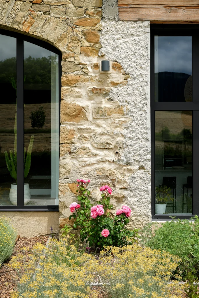 Rénovation complète d’une maison de famille – Drôme
Nichée au cœur des paysages de la Drôme, cette maison a fait l’objet d’une rénovation intégrale. Le projet a consisté à redonner vie à une bâtisse aux volumes autrefois fermés et cloisonnés, pour en révéler tout le potentiel architectural et spatial.
L’intervention a porté sur l’ensemble de l’enveloppe : les façades ont été restaurées, les ouvertures repensées et créées pour offrir de nouveaux cadrages sur le paysage, mettant en valeur la pierre existante et la richesse du contexte environnant.
À l’intérieur, les espaces ont été entièrement réorganisés. Le plan initial, fragmenté et contraint, a laissé place à des enchaînements fluides, où les pièces dialoguent entre elles et s’ouvrent généreusement sur l’extérieur. Chaque ouverture devient un tableau vivant, cadrant une portion de nature : champs de blé, forêt, lumière changeante.
Le cœur de la maison se structure autour de volumes entremêlés. Une cheminée centrale, élément à la fois architectural et domestique, relie les grands volumes de la cuisine en double hauteur et le salon, plus intime et chaleureux. Dans une autre aile, à l’étage, une seconde cuisine a été aménagée. Elle prolonge l’esprit du projet : fonctionnalité discrète, ouverture maîtrisée, cadrages sensibles sur le paysage.
Les ambiances varient selon les espaces : une chambre se déploie autour d’un vide intérieur, jouant avec les hauteurs et les couleurs ; le salon TV, équipé d’une bibliothèque et de rangements intégrés, offre un lieu de retrait, propice au calme tout en restant connecté à l’extérieur.
Le choix des matériaux renforce l’identité sobre et chaleureuse du lieu : pierre naturelle, travertin, parquet en chêne et surfaces en solid surface s’équilibrent pour créer une atmosphère douce, intemporelle et raffinée.
Les ouvertures ont été dessinées pour favoriser la lumière naturelle et créer des liens visuels avec le paysage, tout en accompagnant les usages quotidiens. À l’extérieur, une piscine s’insère discrètement dans le jardin paysager, entourée de terrasses orientées pour profiter du soleil tout au long de la journée. La maison se fond progressivement dans son environnement, entre les cultures et les bois, dans un dialogue apaisé avec le site.
Enfin, les espaces de nuit, regroupés dans une aile plus en retrait, assurent calme et sérénité. Ils sont complétés par une salle de sport et un second salon dédié aux plus jeunes, pour que chacun puisse vivre la maison à son rythme, en toute liberté.