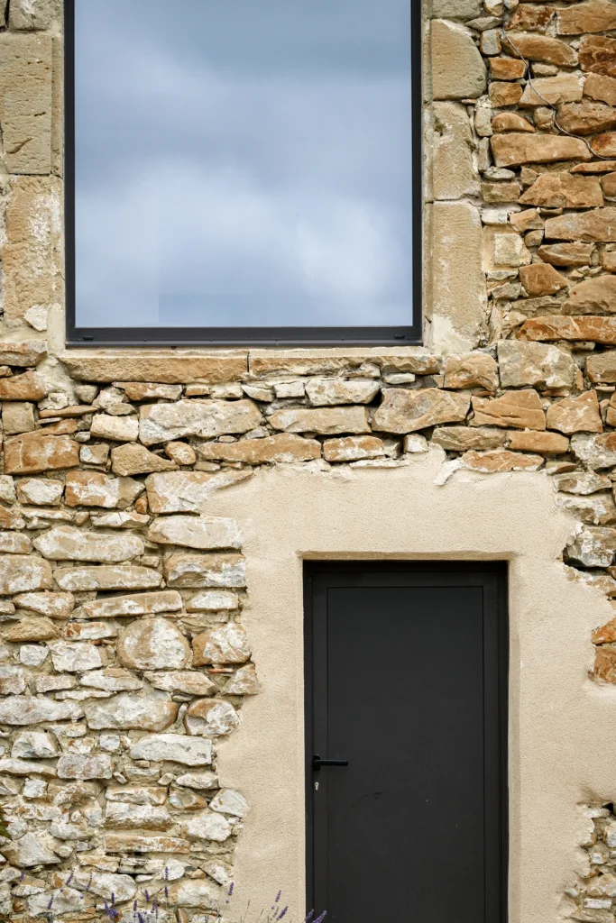 Rénovation complète d’une maison de famille – Drôme
Nichée au cœur des paysages de la Drôme, cette maison a fait l’objet d’une rénovation intégrale. Le projet a consisté à redonner vie à une bâtisse aux volumes autrefois fermés et cloisonnés, pour en révéler tout le potentiel architectural et spatial.
L’intervention a porté sur l’ensemble de l’enveloppe : les façades ont été restaurées, les ouvertures repensées et créées pour offrir de nouveaux cadrages sur le paysage, mettant en valeur la pierre existante et la richesse du contexte environnant.
À l’intérieur, les espaces ont été entièrement réorganisés. Le plan initial, fragmenté et contraint, a laissé place à des enchaînements fluides, où les pièces dialoguent entre elles et s’ouvrent généreusement sur l’extérieur. Chaque ouverture devient un tableau vivant, cadrant une portion de nature : champs de blé, forêt, lumière changeante.
Le cœur de la maison se structure autour de volumes entremêlés. Une cheminée centrale, élément à la fois architectural et domestique, relie les grands volumes de la cuisine en double hauteur et le salon, plus intime et chaleureux. Dans une autre aile, à l’étage, une seconde cuisine a été aménagée. Elle prolonge l’esprit du projet : fonctionnalité discrète, ouverture maîtrisée, cadrages sensibles sur le paysage.
Les ambiances varient selon les espaces : une chambre se déploie autour d’un vide intérieur, jouant avec les hauteurs et les couleurs ; le salon TV, équipé d’une bibliothèque et de rangements intégrés, offre un lieu de retrait, propice au calme tout en restant connecté à l’extérieur.
Le choix des matériaux renforce l’identité sobre et chaleureuse du lieu : pierre naturelle, travertin, parquet en chêne et surfaces en solid surface s’équilibrent pour créer une atmosphère douce, intemporelle et raffinée.
Les ouvertures ont été dessinées pour favoriser la lumière naturelle et créer des liens visuels avec le paysage, tout en accompagnant les usages quotidiens. À l’extérieur, une piscine s’insère discrètement dans le jardin paysager, entourée de terrasses orientées pour profiter du soleil tout au long de la journée. La maison se fond progressivement dans son environnement, entre les cultures et les bois, dans un dialogue apaisé avec le site.
Enfin, les espaces de nuit, regroupés dans une aile plus en retrait, assurent calme et sérénité. Ils sont complétés par une salle de sport et un second salon dédié aux plus jeunes, pour que chacun puisse vivre la maison à son rythme, en toute liberté.