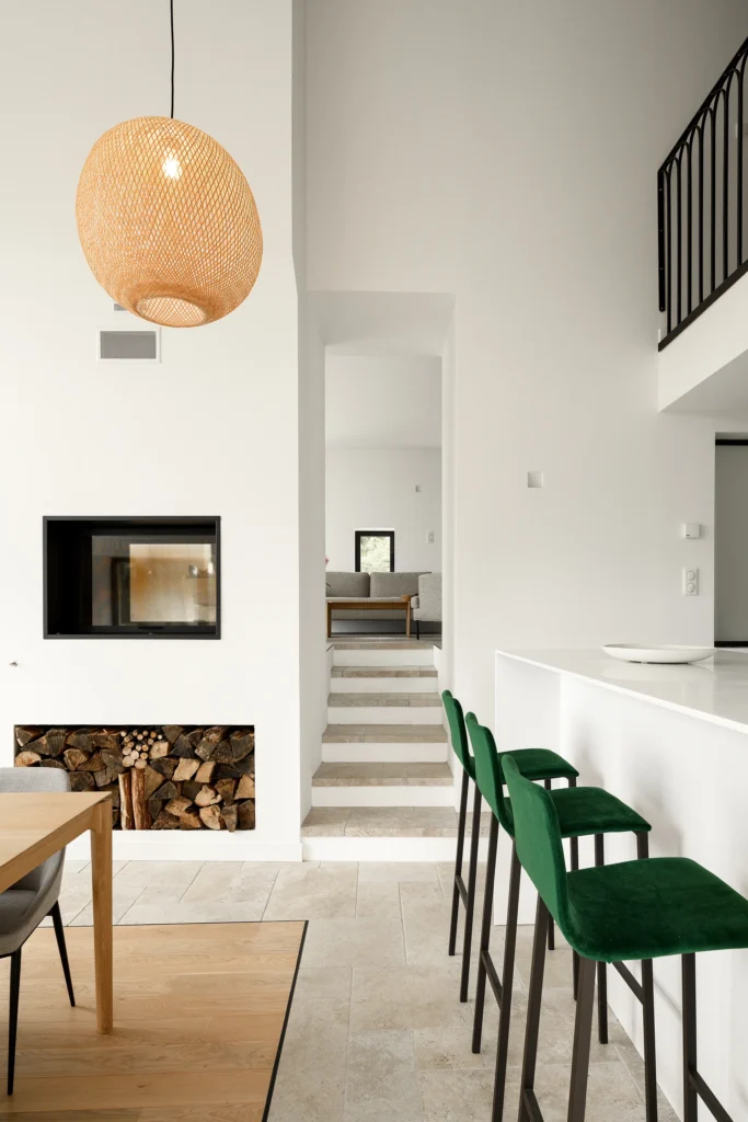 Rénovation complète d’une maison de famille – Drôme
Nichée au cœur des paysages de la Drôme, cette maison a fait l’objet d’une rénovation intégrale. Le projet a consisté à redonner vie à une bâtisse aux volumes autrefois fermés et cloisonnés, pour en révéler tout le potentiel architectural et spatial.
L’intervention a porté sur l’ensemble de l’enveloppe : les façades ont été restaurées, les ouvertures repensées et créées pour offrir de nouveaux cadrages sur le paysage, mettant en valeur la pierre existante et la richesse du contexte environnant.
À l’intérieur, les espaces ont été entièrement réorganisés. Le plan initial, fragmenté et contraint, a laissé place à des enchaînements fluides, où les pièces dialoguent entre elles et s’ouvrent généreusement sur l’extérieur. Chaque ouverture devient un tableau vivant, cadrant une portion de nature : champs de blé, forêt, lumière changeante.
Le cœur de la maison se structure autour de volumes entremêlés. Une cheminée centrale, élément à la fois architectural et domestique, relie les grands volumes de la cuisine en double hauteur et le salon, plus intime et chaleureux. Dans une autre aile, à l’étage, une seconde cuisine a été aménagée. Elle prolonge l’esprit du projet : fonctionnalité discrète, ouverture maîtrisée, cadrages sensibles sur le paysage.
Les ambiances varient selon les espaces : une chambre se déploie autour d’un vide intérieur, jouant avec les hauteurs et les couleurs ; le salon TV, équipé d’une bibliothèque et de rangements intégrés, offre un lieu de retrait, propice au calme tout en restant connecté à l’extérieur.
Le choix des matériaux renforce l’identité sobre et chaleureuse du lieu : pierre naturelle, travertin, parquet en chêne et surfaces en solid surface s’équilibrent pour créer une atmosphère douce, intemporelle et raffinée.
Les ouvertures ont été dessinées pour favoriser la lumière naturelle et créer des liens visuels avec le paysage, tout en accompagnant les usages quotidiens. À l’extérieur, une piscine s’insère discrètement dans le jardin paysager, entourée de terrasses orientées pour profiter du soleil tout au long de la journée. La maison se fond progressivement dans son environnement, entre les cultures et les bois, dans un dialogue apaisé avec le site.
Enfin, les espaces de nuit, regroupés dans une aile plus en retrait, assurent calme et sérénité. Ils sont complétés par une salle de sport et un second salon dédié aux plus jeunes, pour que chacun puisse vivre la maison à son rythme, en toute liberté.