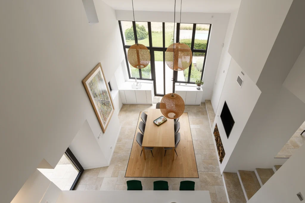 Rénovation complète d’une maison de famille – Drôme
Nichée au cœur des paysages de la Drôme, cette maison a fait l’objet d’une rénovation intégrale. Le projet a consisté à redonner vie à une bâtisse aux volumes autrefois fermés et cloisonnés, pour en révéler tout le potentiel architectural et spatial.
L’intervention a porté sur l’ensemble de l’enveloppe : les façades ont été restaurées, les ouvertures repensées et créées pour offrir de nouveaux cadrages sur le paysage, mettant en valeur la pierre existante et la richesse du contexte environnant.
À l’intérieur, les espaces ont été entièrement réorganisés. Le plan initial, fragmenté et contraint, a laissé place à des enchaînements fluides, où les pièces dialoguent entre elles et s’ouvrent généreusement sur l’extérieur. Chaque ouverture devient un tableau vivant, cadrant une portion de nature : champs de blé, forêt, lumière changeante.
Le cœur de la maison se structure autour de volumes entremêlés. Une cheminée centrale, élément à la fois architectural et domestique, relie les grands volumes de la cuisine en double hauteur et le salon, plus intime et chaleureux. Dans une autre aile, à l’étage, une seconde cuisine a été aménagée. Elle prolonge l’esprit du projet : fonctionnalité discrète, ouverture maîtrisée, cadrages sensibles sur le paysage.
Les ambiances varient selon les espaces : une chambre se déploie autour d’un vide intérieur, jouant avec les hauteurs et les couleurs ; le salon TV, équipé d’une bibliothèque et de rangements intégrés, offre un lieu de retrait, propice au calme tout en restant connecté à l’extérieur.
Le choix des matériaux renforce l’identité sobre et chaleureuse du lieu : pierre naturelle, travertin, parquet en chêne et surfaces en solid surface s’équilibrent pour créer une atmosphère douce, intemporelle et raffinée.
Les ouvertures ont été dessinées pour favoriser la lumière naturelle et créer des liens visuels avec le paysage, tout en accompagnant les usages quotidiens. À l’extérieur, une piscine s’insère discrètement dans le jardin paysager, entourée de terrasses orientées pour profiter du soleil tout au long de la journée. La maison se fond progressivement dans son environnement, entre les cultures et les bois, dans un dialogue apaisé avec le site.
Enfin, les espaces de nuit, regroupés dans une aile plus en retrait, assurent calme et sérénité. Ils sont complétés par une salle de sport et un second salon dédié aux plus jeunes, pour que chacun puisse vivre la maison à son rythme, en toute liberté.