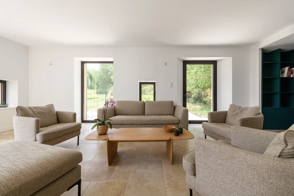 Rénovation complète d’une maison de famille – Drôme
Nichée au cœur des paysages de la Drôme, cette maison a fait l’objet d’une rénovation intégrale. Le projet a consisté à redonner vie à une bâtisse aux volumes autrefois fermés et cloisonnés, pour en révéler tout le potentiel architectural et spatial.
L’intervention a porté sur l’ensemble de l’enveloppe : les façades ont été restaurées, les ouvertures repensées et créées pour offrir de nouveaux cadrages sur le paysage, mettant en valeur la pierre existante et la richesse du contexte environnant.
À l’intérieur, les espaces ont été entièrement réorganisés. Le plan initial, fragmenté et contraint, a laissé place à des enchaînements fluides, où les pièces dialoguent entre elles et s’ouvrent généreusement sur l’extérieur. Chaque ouverture devient un tableau vivant, cadrant une portion de nature : champs de blé, forêt, lumière changeante.
Le cœur de la maison se structure autour de volumes entremêlés. Une cheminée centrale, élément à la fois architectural et domestique, relie les grands volumes de la cuisine en double hauteur et le salon, plus intime et chaleureux. Dans une autre aile, à l’étage, une seconde cuisine a été aménagée. Elle prolonge l’esprit du projet : fonctionnalité discrète, ouverture maîtrisée, cadrages sensibles sur le paysage.
Les ambiances varient selon les espaces : une chambre se déploie autour d’un vide intérieur, jouant avec les hauteurs et les couleurs ; le salon TV, équipé d’une bibliothèque et de rangements intégrés, offre un lieu de retrait, propice au calme tout en restant connecté à l’extérieur.
Le choix des matériaux renforce l’identité sobre et chaleureuse du lieu : pierre naturelle, travertin, parquet en chêne et surfaces en solid surface s’équilibrent pour créer une atmosphère douce, intemporelle et raffinée.
Les ouvertures ont été dessinées pour favoriser la lumière naturelle et créer des liens visuels avec le paysage, tout en accompagnant les usages quotidiens. À l’extérieur, une piscine s’insère discrètement dans le jardin paysager, entourée de terrasses orientées pour profiter du soleil tout au long de la journée. La maison se fond progressivement dans son environnement, entre les cultures et les bois, dans un dialogue apaisé avec le site.
Enfin, les espaces de nuit, regroupés dans une aile plus en retrait, assurent calme et sérénité. Ils sont complétés par une salle de sport et un second salon dédié aux plus jeunes, pour que chacun puisse vivre la maison à son rythme, en toute liberté.