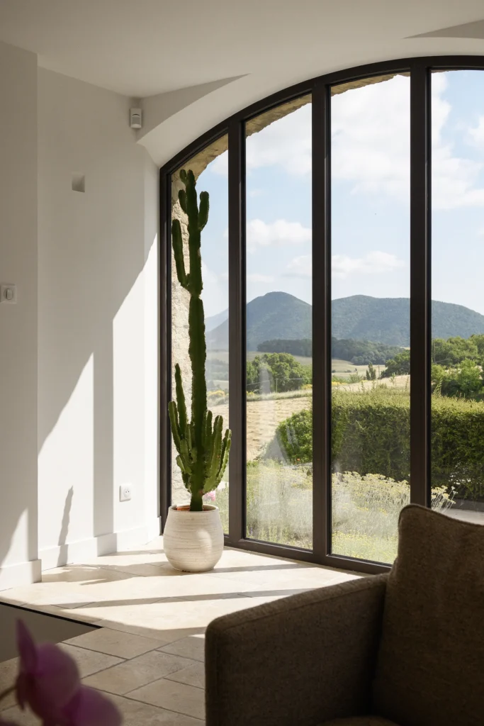 Rénovation complète d’une maison de famille – Drôme
Nichée au cœur des paysages de la Drôme, cette maison a fait l’objet d’une rénovation intégrale. Le projet a consisté à redonner vie à une bâtisse aux volumes autrefois fermés et cloisonnés, pour en révéler tout le potentiel architectural et spatial.
L’intervention a porté sur l’ensemble de l’enveloppe : les façades ont été restaurées, les ouvertures repensées et créées pour offrir de nouveaux cadrages sur le paysage, mettant en valeur la pierre existante et la richesse du contexte environnant.
À l’intérieur, les espaces ont été entièrement réorganisés. Le plan initial, fragmenté et contraint, a laissé place à des enchaînements fluides, où les pièces dialoguent entre elles et s’ouvrent généreusement sur l’extérieur. Chaque ouverture devient un tableau vivant, cadrant une portion de nature : champs de blé, forêt, lumière changeante.
Le cœur de la maison se structure autour de volumes entremêlés. Une cheminée centrale, élément à la fois architectural et domestique, relie les grands volumes de la cuisine en double hauteur et le salon, plus intime et chaleureux. Dans une autre aile, à l’étage, une seconde cuisine a été aménagée. Elle prolonge l’esprit du projet : fonctionnalité discrète, ouverture maîtrisée, cadrages sensibles sur le paysage.
Les ambiances varient selon les espaces : une chambre se déploie autour d’un vide intérieur, jouant avec les hauteurs et les couleurs ; le salon TV, équipé d’une bibliothèque et de rangements intégrés, offre un lieu de retrait, propice au calme tout en restant connecté à l’extérieur.
Le choix des matériaux renforce l’identité sobre et chaleureuse du lieu : pierre naturelle, travertin, parquet en chêne et surfaces en solid surface s’équilibrent pour créer une atmosphère douce, intemporelle et raffinée.
Les ouvertures ont été dessinées pour favoriser la lumière naturelle et créer des liens visuels avec le paysage, tout en accompagnant les usages quotidiens. À l’extérieur, une piscine s’insère discrètement dans le jardin paysager, entourée de terrasses orientées pour profiter du soleil tout au long de la journée. La maison se fond progressivement dans son environnement, entre les cultures et les bois, dans un dialogue apaisé avec le site.
Enfin, les espaces de nuit, regroupés dans une aile plus en retrait, assurent calme et sérénité. Ils sont complétés par une salle de sport et un second salon dédié aux plus jeunes, pour que chacun puisse vivre la maison à son rythme, en toute liberté.