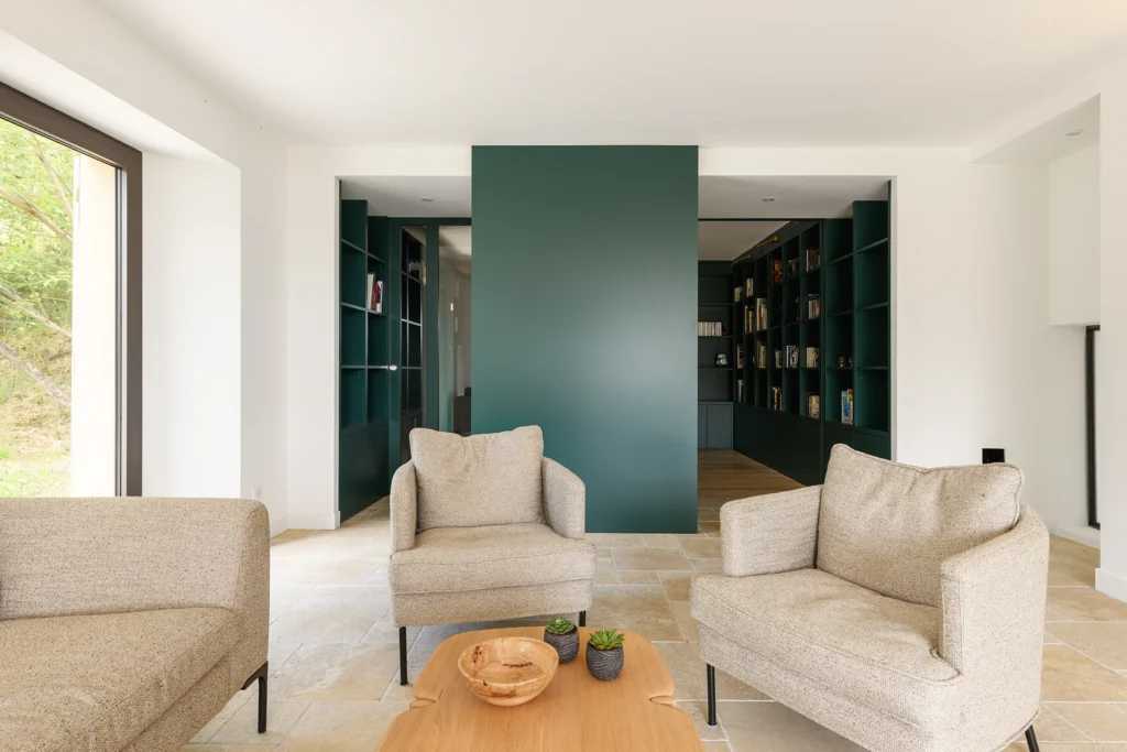 Rénovation complète d’une maison de famille – Drôme
Nichée au cœur des paysages de la Drôme, cette maison a fait l’objet d’une rénovation intégrale. Le projet a consisté à redonner vie à une bâtisse aux volumes autrefois fermés et cloisonnés, pour en révéler tout le potentiel architectural et spatial.
L’intervention a porté sur l’ensemble de l’enveloppe : les façades ont été restaurées, les ouvertures repensées et créées pour offrir de nouveaux cadrages sur le paysage, mettant en valeur la pierre existante et la richesse du contexte environnant.
À l’intérieur, les espaces ont été entièrement réorganisés. Le plan initial, fragmenté et contraint, a laissé place à des enchaînements fluides, où les pièces dialoguent entre elles et s’ouvrent généreusement sur l’extérieur. Chaque ouverture devient un tableau vivant, cadrant une portion de nature : champs de blé, forêt, lumière changeante.
Le cœur de la maison se structure autour de volumes entremêlés. Une cheminée centrale, élément à la fois architectural et domestique, relie les grands volumes de la cuisine en double hauteur et le salon, plus intime et chaleureux. Dans une autre aile, à l’étage, une seconde cuisine a été aménagée. Elle prolonge l’esprit du projet : fonctionnalité discrète, ouverture maîtrisée, cadrages sensibles sur le paysage.
Les ambiances varient selon les espaces : une chambre se déploie autour d’un vide intérieur, jouant avec les hauteurs et les couleurs ; le salon TV, équipé d’une bibliothèque et de rangements intégrés, offre un lieu de retrait, propice au calme tout en restant connecté à l’extérieur.
Le choix des matériaux renforce l’identité sobre et chaleureuse du lieu : pierre naturelle, travertin, parquet en chêne et surfaces en solid surface s’équilibrent pour créer une atmosphère douce, intemporelle et raffinée.
Les ouvertures ont été dessinées pour favoriser la lumière naturelle et créer des liens visuels avec le paysage, tout en accompagnant les usages quotidiens. À l’extérieur, une piscine s’insère discrètement dans le jardin paysager, entourée de terrasses orientées pour profiter du soleil tout au long de la journée. La maison se fond progressivement dans son environnement, entre les cultures et les bois, dans un dialogue apaisé avec le site.
Enfin, les espaces de nuit, regroupés dans une aile plus en retrait, assurent calme et sérénité. Ils sont complétés par une salle de sport et un second salon dédié aux plus jeunes, pour que chacun puisse vivre la maison à son rythme, en toute liberté.