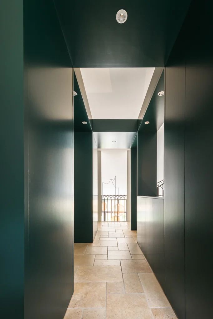Rénovation complète d’une maison de famille – Drôme
Nichée au cœur des paysages de la Drôme, cette maison a fait l’objet d’une rénovation intégrale. Le projet a consisté à redonner vie à une bâtisse aux volumes autrefois fermés et cloisonnés, pour en révéler tout le potentiel architectural et spatial.
L’intervention a porté sur l’ensemble de l’enveloppe : les façades ont été restaurées, les ouvertures repensées et créées pour offrir de nouveaux cadrages sur le paysage, mettant en valeur la pierre existante et la richesse du contexte environnant.
À l’intérieur, les espaces ont été entièrement réorganisés. Le plan initial, fragmenté et contraint, a laissé place à des enchaînements fluides, où les pièces dialoguent entre elles et s’ouvrent généreusement sur l’extérieur. Chaque ouverture devient un tableau vivant, cadrant une portion de nature : champs de blé, forêt, lumière changeante.
Le cœur de la maison se structure autour de volumes entremêlés. Une cheminée centrale, élément à la fois architectural et domestique, relie les grands volumes de la cuisine en double hauteur et le salon, plus intime et chaleureux. Dans une autre aile, à l’étage, une seconde cuisine a été aménagée. Elle prolonge l’esprit du projet : fonctionnalité discrète, ouverture maîtrisée, cadrages sensibles sur le paysage.
Les ambiances varient selon les espaces : une chambre se déploie autour d’un vide intérieur, jouant avec les hauteurs et les couleurs ; le salon TV, équipé d’une bibliothèque et de rangements intégrés, offre un lieu de retrait, propice au calme tout en restant connecté à l’extérieur.
Le choix des matériaux renforce l’identité sobre et chaleureuse du lieu : pierre naturelle, travertin, parquet en chêne et surfaces en solid surface s’équilibrent pour créer une atmosphère douce, intemporelle et raffinée.
Les ouvertures ont été dessinées pour favoriser la lumière naturelle et créer des liens visuels avec le paysage, tout en accompagnant les usages quotidiens. À l’extérieur, une piscine s’insère discrètement dans le jardin paysager, entourée de terrasses orientées pour profiter du soleil tout au long de la journée. La maison se fond progressivement dans son environnement, entre les cultures et les bois, dans un dialogue apaisé avec le site.
Enfin, les espaces de nuit, regroupés dans une aile plus en retrait, assurent calme et sérénité. Ils sont complétés par une salle de sport et un second salon dédié aux plus jeunes, pour que chacun puisse vivre la maison à son rythme, en toute liberté.
