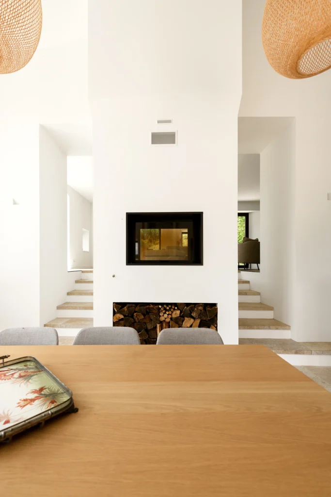 Rénovation complète d’une maison de famille – Drôme
Nichée au cœur des paysages de la Drôme, cette maison a fait l’objet d’une rénovation intégrale. Le projet a consisté à redonner vie à une bâtisse aux volumes autrefois fermés et cloisonnés, pour en révéler tout le potentiel architectural et spatial.
L’intervention a porté sur l’ensemble de l’enveloppe : les façades ont été restaurées, les ouvertures repensées et créées pour offrir de nouveaux cadrages sur le paysage, mettant en valeur la pierre existante et la richesse du contexte environnant.
À l’intérieur, les espaces ont été entièrement réorganisés. Le plan initial, fragmenté et contraint, a laissé place à des enchaînements fluides, où les pièces dialoguent entre elles et s’ouvrent généreusement sur l’extérieur. Chaque ouverture devient un tableau vivant, cadrant une portion de nature : champs de blé, forêt, lumière changeante.
Le cœur de la maison se structure autour de volumes entremêlés. Une cheminée centrale, élément à la fois architectural et domestique, relie les grands volumes de la cuisine en double hauteur et le salon, plus intime et chaleureux. Dans une autre aile, à l’étage, une seconde cuisine a été aménagée. Elle prolonge l’esprit du projet : fonctionnalité discrète, ouverture maîtrisée, cadrages sensibles sur le paysage.
Les ambiances varient selon les espaces : une chambre se déploie autour d’un vide intérieur, jouant avec les hauteurs et les couleurs ; le salon TV, équipé d’une bibliothèque et de rangements intégrés, offre un lieu de retrait, propice au calme tout en restant connecté à l’extérieur.
Le choix des matériaux renforce l’identité sobre et chaleureuse du lieu : pierre naturelle, travertin, parquet en chêne et surfaces en solid surface s’équilibrent pour créer une atmosphère douce, intemporelle et raffinée.
Les ouvertures ont été dessinées pour favoriser la lumière naturelle et créer des liens visuels avec le paysage, tout en accompagnant les usages quotidiens. À l’extérieur, une piscine s’insère discrètement dans le jardin paysager, entourée de terrasses orientées pour profiter du soleil tout au long de la journée. La maison se fond progressivement dans son environnement, entre les cultures et les bois, dans un dialogue apaisé avec le site.
Enfin, les espaces de nuit, regroupés dans une aile plus en retrait, assurent calme et sérénité. Ils sont complétés par une salle de sport et un second salon dédié aux plus jeunes, pour que chacun puisse vivre la maison à son rythme, en toute liberté.