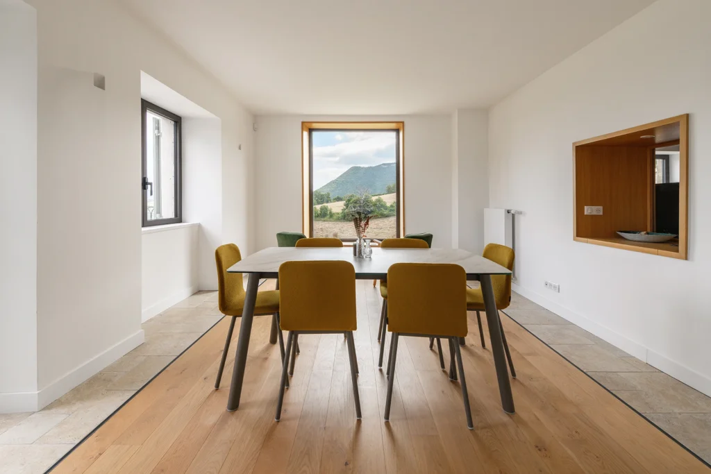 Rénovation complète d’une maison de famille – Drôme
Nichée au cœur des paysages de la Drôme, cette maison a fait l’objet d’une rénovation intégrale. Le projet a consisté à redonner vie à une bâtisse aux volumes autrefois fermés et cloisonnés, pour en révéler tout le potentiel architectural et spatial.
L’intervention a porté sur l’ensemble de l’enveloppe : les façades ont été restaurées, les ouvertures repensées et créées pour offrir de nouveaux cadrages sur le paysage, mettant en valeur la pierre existante et la richesse du contexte environnant.
À l’intérieur, les espaces ont été entièrement réorganisés. Le plan initial, fragmenté et contraint, a laissé place à des enchaînements fluides, où les pièces dialoguent entre elles et s’ouvrent généreusement sur l’extérieur. Chaque ouverture devient un tableau vivant, cadrant une portion de nature : champs de blé, forêt, lumière changeante.
Le cœur de la maison se structure autour de volumes entremêlés. Une cheminée centrale, élément à la fois architectural et domestique, relie les grands volumes de la cuisine en double hauteur et le salon, plus intime et chaleureux. Dans une autre aile, à l’étage, une seconde cuisine a été aménagée. Elle prolonge l’esprit du projet : fonctionnalité discrète, ouverture maîtrisée, cadrages sensibles sur le paysage.
Les ambiances varient selon les espaces : une chambre se déploie autour d’un vide intérieur, jouant avec les hauteurs et les couleurs ; le salon TV, équipé d’une bibliothèque et de rangements intégrés, offre un lieu de retrait, propice au calme tout en restant connecté à l’extérieur.
Le choix des matériaux renforce l’identité sobre et chaleureuse du lieu : pierre naturelle, travertin, parquet en chêne et surfaces en solid surface s’équilibrent pour créer une atmosphère douce, intemporelle et raffinée.
Les ouvertures ont été dessinées pour favoriser la lumière naturelle et créer des liens visuels avec le paysage, tout en accompagnant les usages quotidiens. À l’extérieur, une piscine s’insère discrètement dans le jardin paysager, entourée de terrasses orientées pour profiter du soleil tout au long de la journée. La maison se fond progressivement dans son environnement, entre les cultures et les bois, dans un dialogue apaisé avec le site.
Enfin, les espaces de nuit, regroupés dans une aile plus en retrait, assurent calme et sérénité. Ils sont complétés par une salle de sport et un second salon dédié aux plus jeunes, pour que chacun puisse vivre la maison à son rythme, en toute liberté.