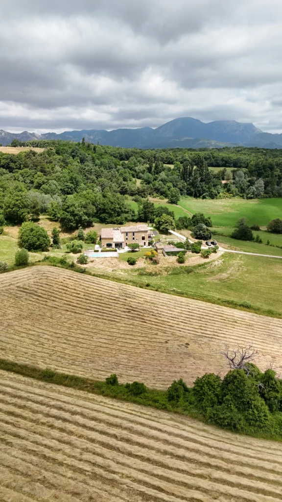 Rénovation complète d’une maison de famille – Drôme
Nichée au cœur des paysages de la Drôme, cette maison a fait l’objet d’une rénovation intégrale. Le projet a consisté à redonner vie à une bâtisse aux volumes autrefois fermés et cloisonnés, pour en révéler tout le potentiel architectural et spatial.
L’intervention a porté sur l’ensemble de l’enveloppe : les façades ont été restaurées, les ouvertures repensées et créées pour offrir de nouveaux cadrages sur le paysage, mettant en valeur la pierre existante et la richesse du contexte environnant.
À l’intérieur, les espaces ont été entièrement réorganisés. Le plan initial, fragmenté et contraint, a laissé place à des enchaînements fluides, où les pièces dialoguent entre elles et s’ouvrent généreusement sur l’extérieur. Chaque ouverture devient un tableau vivant, cadrant une portion de nature : champs de blé, forêt, lumière changeante.
Le cœur de la maison se structure autour de volumes entremêlés. Une cheminée centrale, élément à la fois architectural et domestique, relie les grands volumes de la cuisine en double hauteur et le salon, plus intime et chaleureux. Dans une autre aile, à l’étage, une seconde cuisine a été aménagée. Elle prolonge l’esprit du projet : fonctionnalité discrète, ouverture maîtrisée, cadrages sensibles sur le paysage.
Les ambiances varient selon les espaces : une chambre se déploie autour d’un vide intérieur, jouant avec les hauteurs et les couleurs ; le salon TV, équipé d’une bibliothèque et de rangements intégrés, offre un lieu de retrait, propice au calme tout en restant connecté à l’extérieur.
Le choix des matériaux renforce l’identité sobre et chaleureuse du lieu : pierre naturelle, travertin, parquet en chêne et surfaces en solid surface s’équilibrent pour créer une atmosphère douce, intemporelle et raffinée.
Les ouvertures ont été dessinées pour favoriser la lumière naturelle et créer des liens visuels avec le paysage, tout en accompagnant les usages quotidiens. À l’extérieur, une piscine s’insère discrètement dans le jardin paysager, entourée de terrasses orientées pour profiter du soleil tout au long de la journée. La maison se fond progressivement dans son environnement, entre les cultures et les bois, dans un dialogue apaisé avec le site.
Enfin, les espaces de nuit, regroupés dans une aile plus en retrait, assurent calme et sérénité. Ils sont complétés par une salle de sport et un second salon dédié aux plus jeunes, pour que chacun puisse vivre la maison à son rythme, en toute liberté.