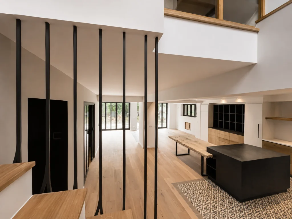 Cuisine contemporaine ouverte sur un vaste séjour, avec îlot noir, mobilier en bois, verrière intérieure et structure métallique sur mesure.