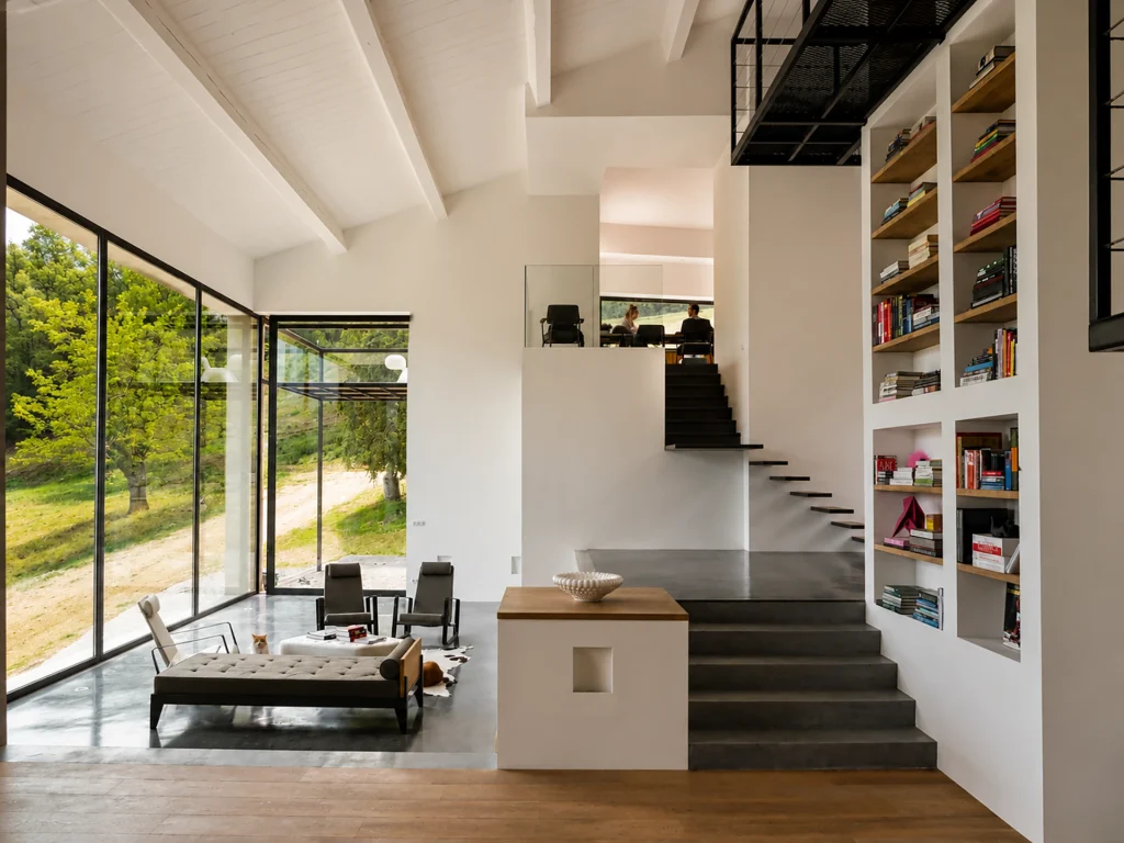 Salon en double hauteur baigné de lumière, avec grandes baies vitrées, bibliothèque intégrée, passerelle métallique et espaces ouverts sur plusieurs niveaux.