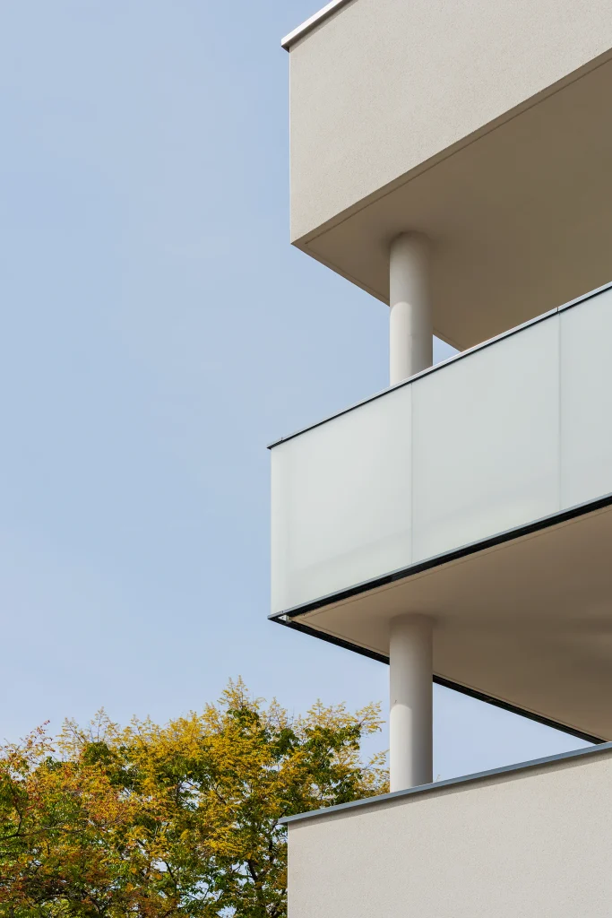 Détail architectural des balcons de la résidence Résiden’Ciel à Valence, conçue par l’Atelier TDR. Les garde-corps en verre opalescent, associés aux poteaux cylindriques et aux lignes épurées des dalles, apportent légèreté et transparence à la façade. Le cadrage souligne le jeu de superposition des volumes et le dialogue entre l’architecture contemporaine et la végétation environnante.