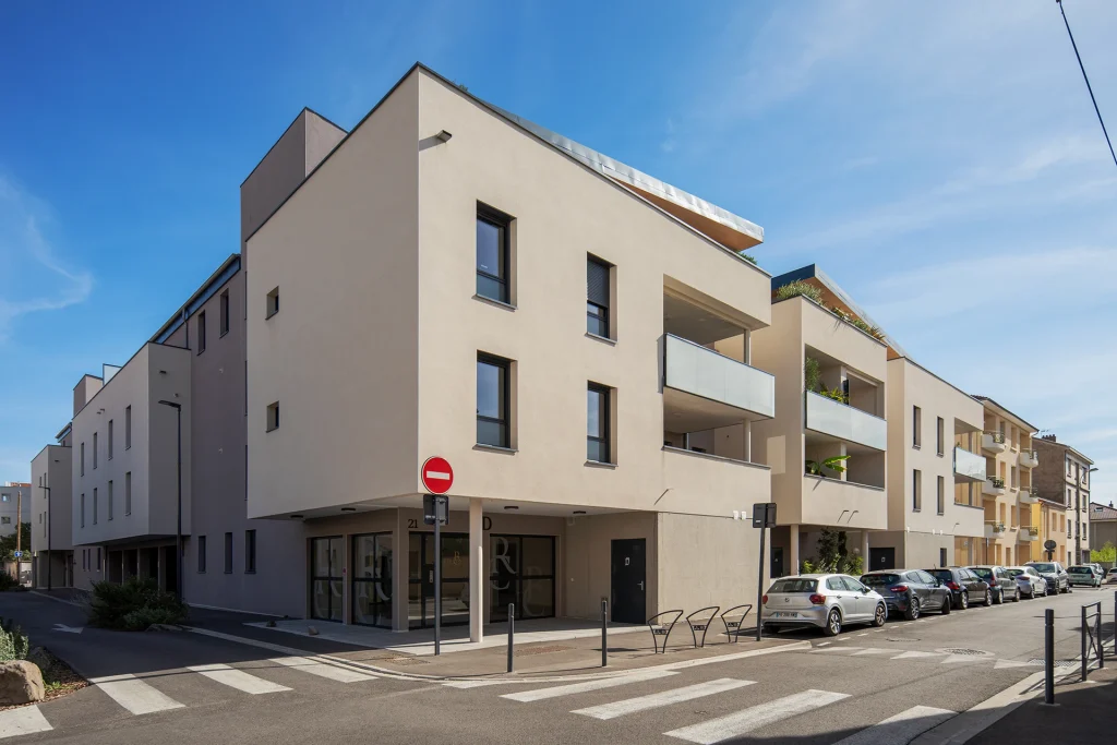 Vue urbaine montrant le traitement de l’angle, la continuité bâtie et les retraits successifs qui allègent le volume de la résidence.