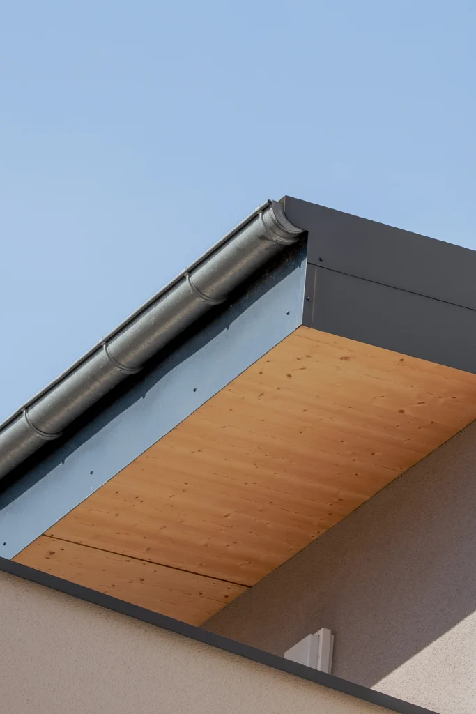 Détail architectural mettant en valeur le dessin de la toiture et la sous-face bois, élément chaleureux contrastant avec la sobriété des façades.