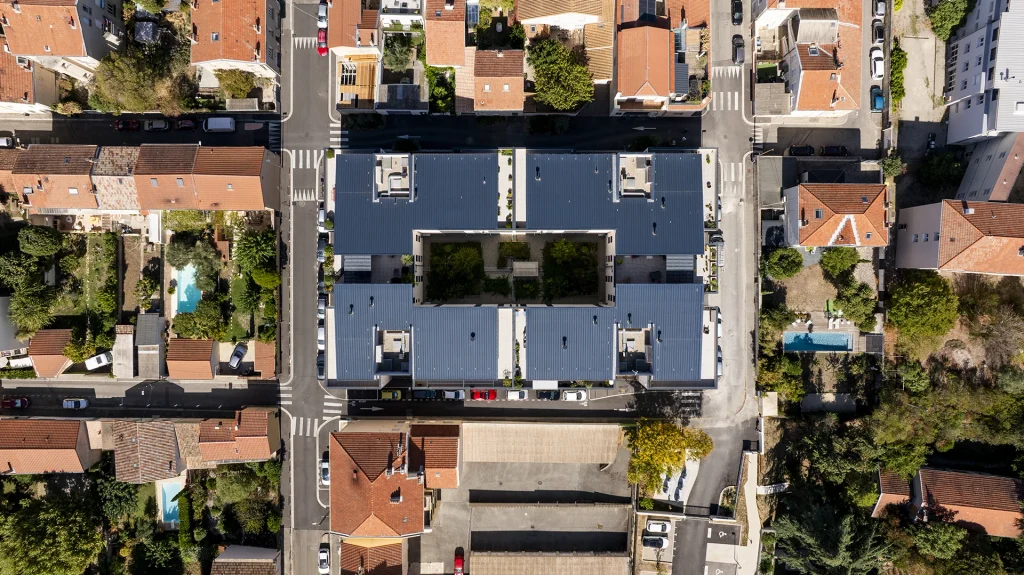 Vue aérienne de la résidence Résiden’Ciel, conçue par l’Atelier TDR à Valence. Cette prise de vue révèle l’organisation du projet autour d’un cœur d’îlot paysager, ainsi que son insertion dans le tissu urbain existant. La composition des volumes, des toitures et des terrasses dessine un ensemble résidentiel structuré, ouvert sur un espace végétalisé central.